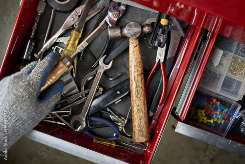 a man opening a tool drawer and holding a chisel inside a workshop.