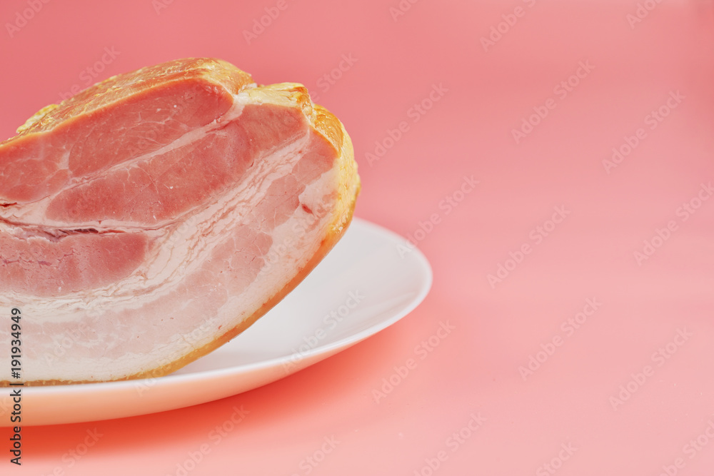 a large fatty piece of smoked bacon lies on plates on a pink background a large fatty piece of smoked bacon lies on plates on a pink background