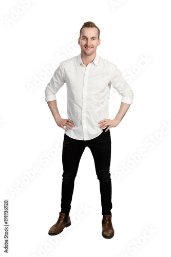 Handsome man standing in front of a white background wearing a white shirt and black jeans looking at camera.