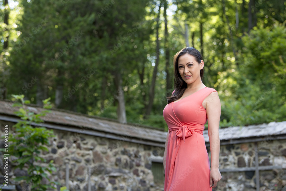 Stunning biracial (Asian and Caucasian) woman poses in garden in pink sun dress Stunning biracial (Asian and Caucasian) woman poses in garden in pink sun dress