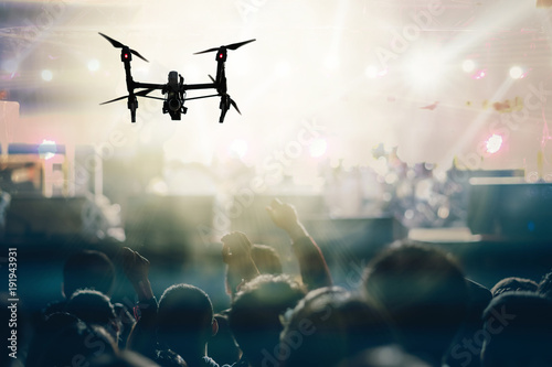 Closeup silhouette of Drone flying for taking video of Concert crowd and Music fanclub with show hand action which follow up the songer at the front of stage, musical and concert concept