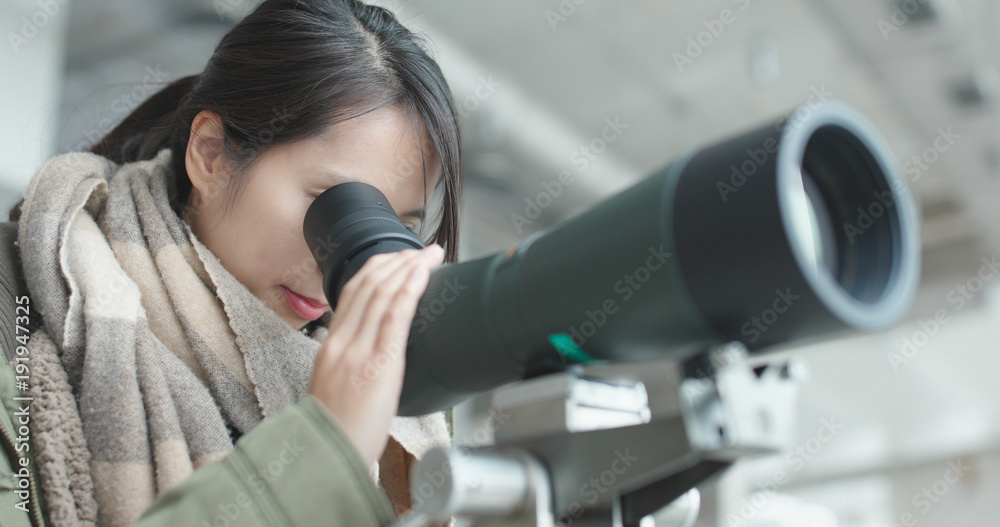 Woman looking through telescope to observe the bird