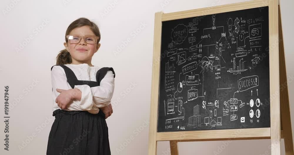 A happy little girl dressed as a teacher in front of a small blackboard ...