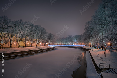 Beautiful view of Aura river with frost covered oak trees on the sides illuminated by streetlight and Turku Cathedral faintly seen in the background in Turku, Finland © Jamo Images