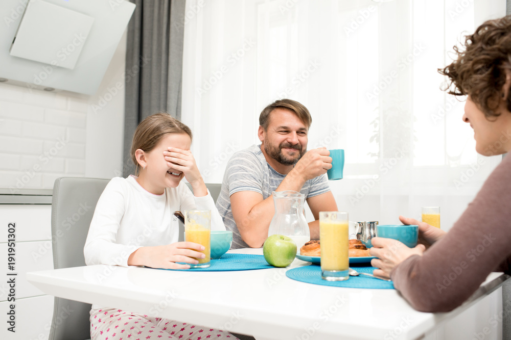 Portrait of carefree young family laughing happily while enjoying breakfast at home sitting at dinner table in cozy kitchen in morning, drinking orange juice Portrait of carefree young family laughing happily while enjoying breakfast at home sitting at dinner table in cozy kitchen in morning, drinking orange juice