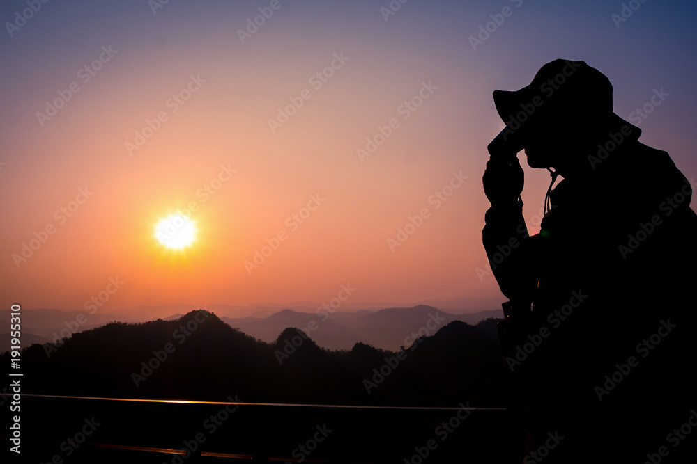 Silhouette Handsome man looking forward with binoculars at a mountain and drinking coffee