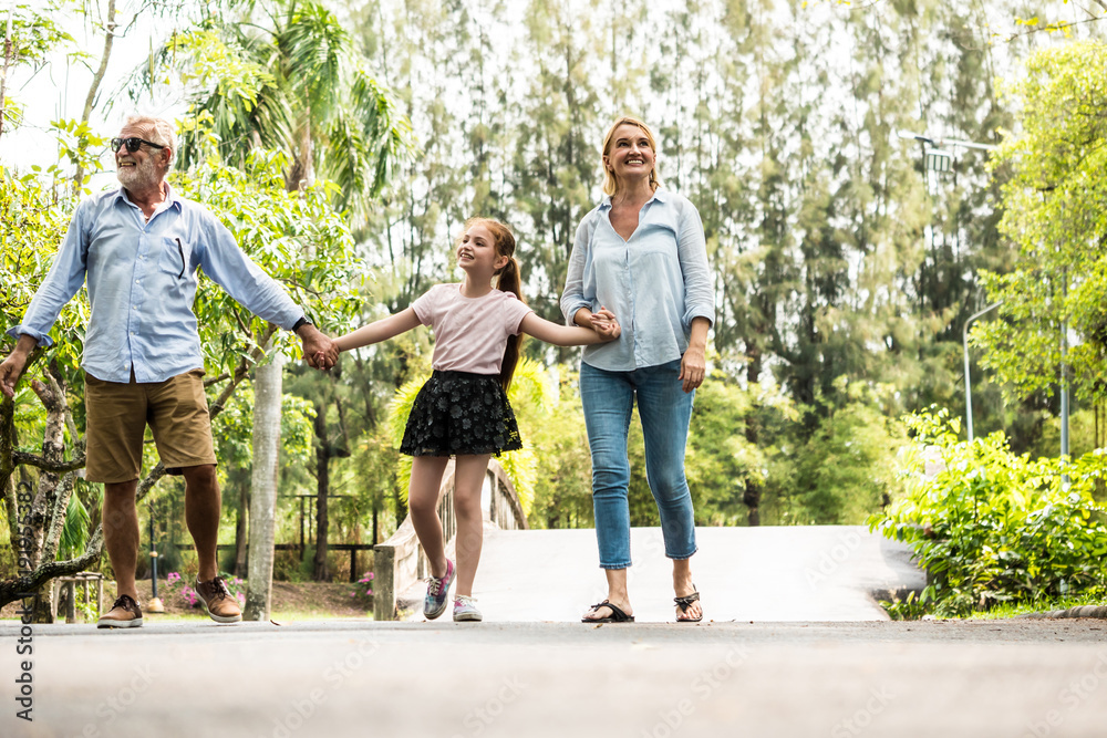 Fototapeta premium Happy family having fun together in the garden. Father, mother and daughter holding hands and walking in a park. Lifestyle concept