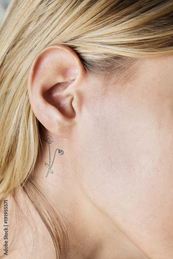 Closeup of a simple behind the ear tattoo of a young woman Closeup of a simple behind the ear tattoo of a young woman