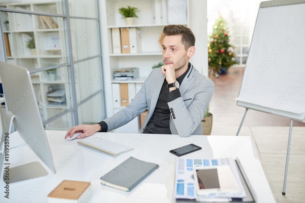 Portrait of modern business manager sitting at desk and using computer while doing internet research in office Portrait of modern business manager sitting at desk and using computer while doing internet research in office