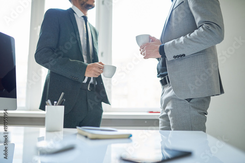 Mid-section portrait of two successful business people holding cups and chatting during coffee break in modern office