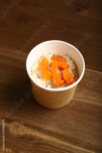 Low-calorie porridge for a healthy diet and lifestyle. Delivery to the house in a paper cup, container. Packaging made from natural materials. Barley with pieces of orange pumpkin. View from above