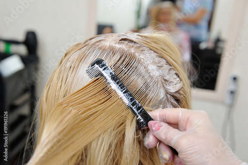 The hairdresser smears the paint on his hair with a comb, for coloring the blonde.