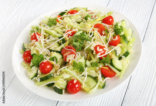 delicious fresh orzo salad with cucumber slices, celery sticks, tomato and bean sprouts on white plate on wooden table, healthy recipe,horizontal view from above, close-up