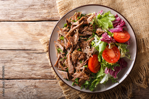 Delicious food: slow cooked pulled beef with fresh vegetable salad close-up. Horizontal top view from above