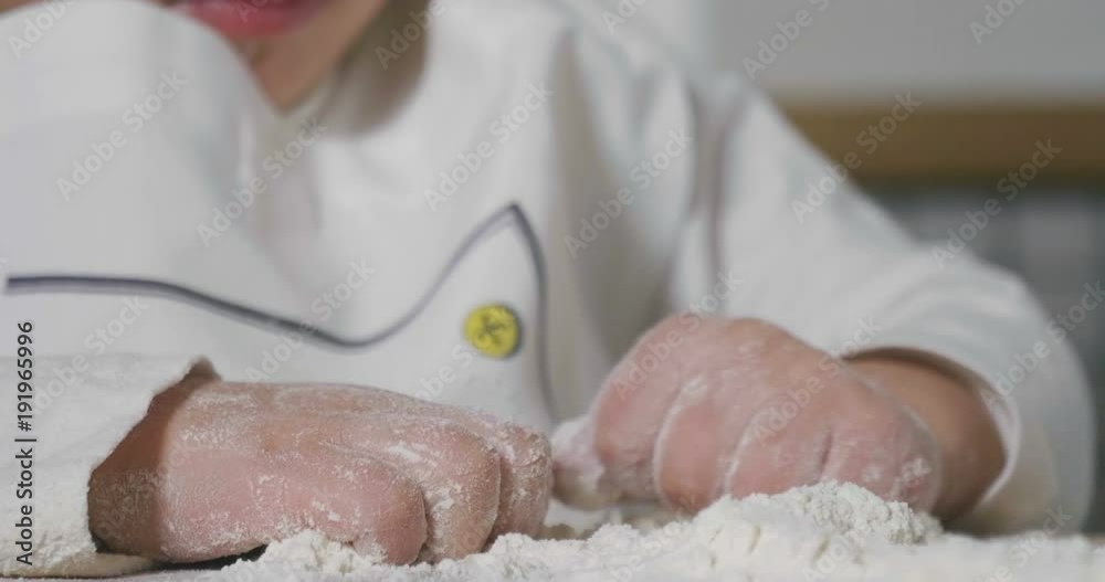 Portrait of a little girl in the kitchen dressed as a professional cook playing with flour, gets her hands dirty and smiles happy. Concept of: nutrition, cooking school, education and game. Portrait of a little girl in the kitchen dressed as a professional cook playing with flour, gets her hands dirty and smiles happy. Concept of: nutrition, cooking school, education and game.