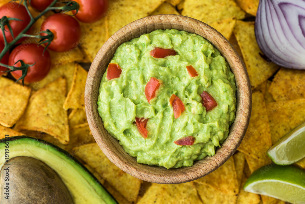Guacamole in Wooden Bowl with Tortilla Chips and Ingredients. Overhead View.