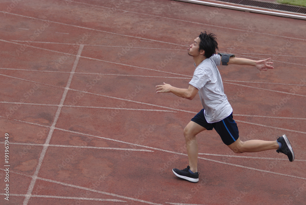 Side view of athletic handsome young Asian runner sprinter crossing the finish line on track in stadium.