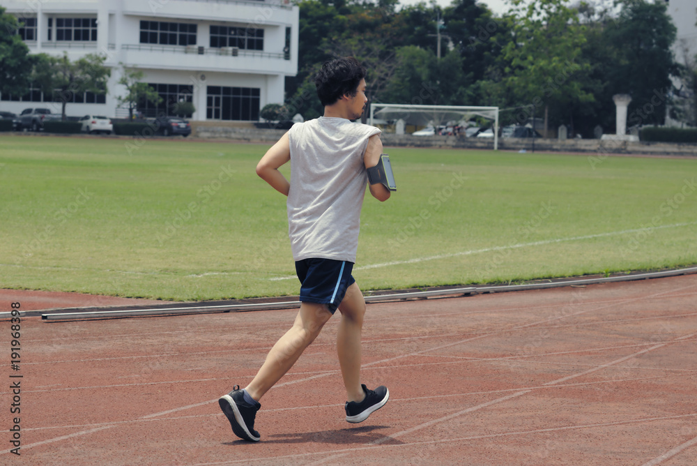 Back view of young athlete Asian man running on racetrack in stadium. Healthy active lifestyle concept.