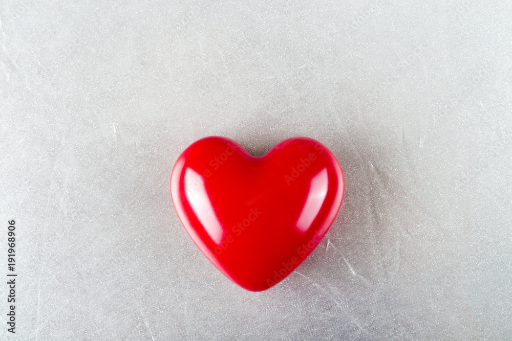 Red glossy heart on silver texture background.