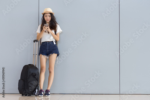 Asian woman teenager using smartphone at airport terminal standingwith luggage suitcase and backpack for travel in vacation summer relaxing waiting flight transport online check in or booking ticket photo