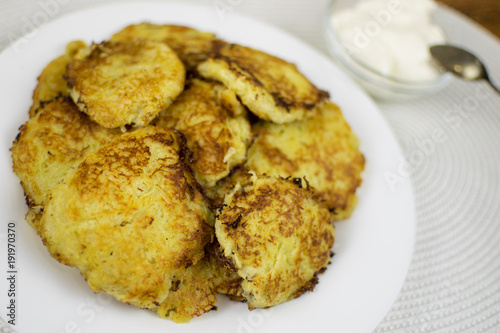 Fried potato pancakes on a white plate and sour cream.