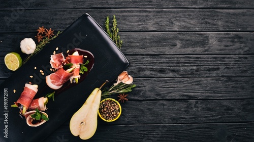 Prosciutto with pear and berry sauce. Cold snacks. Top view. On a black wooden background. Copy space.