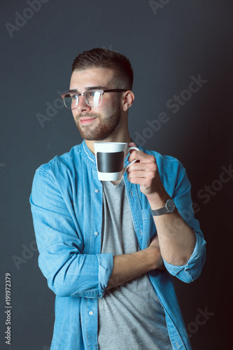 Portrait of a handsome young man standing and holding a cup of coffee in his hands