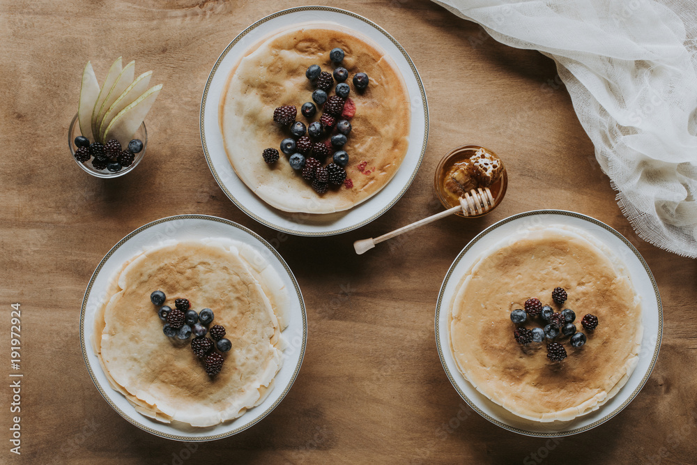 top view of sweet homemade pancakes with berries and honey on wooden table