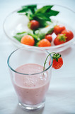 Strawberry milkshake in glass garnished with fresh strawberries on white background