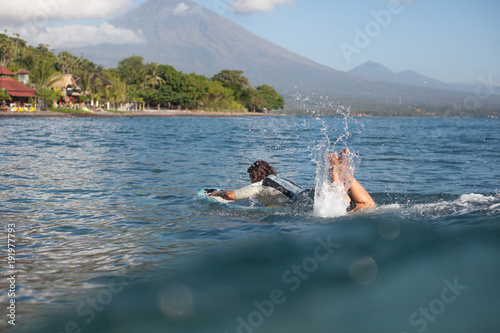 girl lying on surf board in ocean, coastline on background © LIGHTFIELD STUDIOS