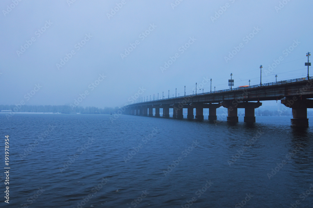 Kyiv winter cityscape with Paton bridge over Dnieper river. Foggy morning view. A few minutes before the snowfall