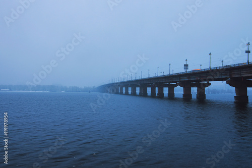 Kyiv winter cityscape with Paton bridge over Dnieper river. Foggy morning view. A few minutes before the snowfall