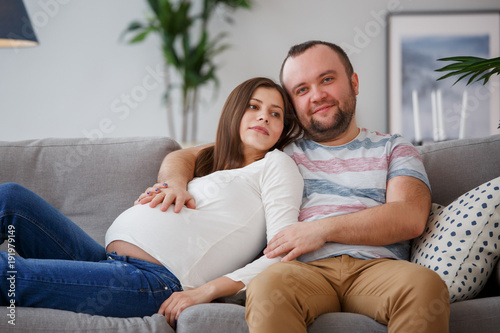 Picture of happy future parents sitting on gray sofa