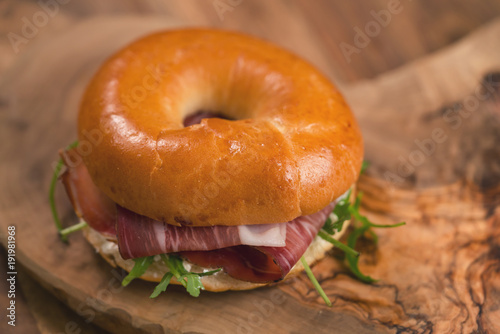 bagel sandwich with prosciutto and cream cheese on wood board with copy space