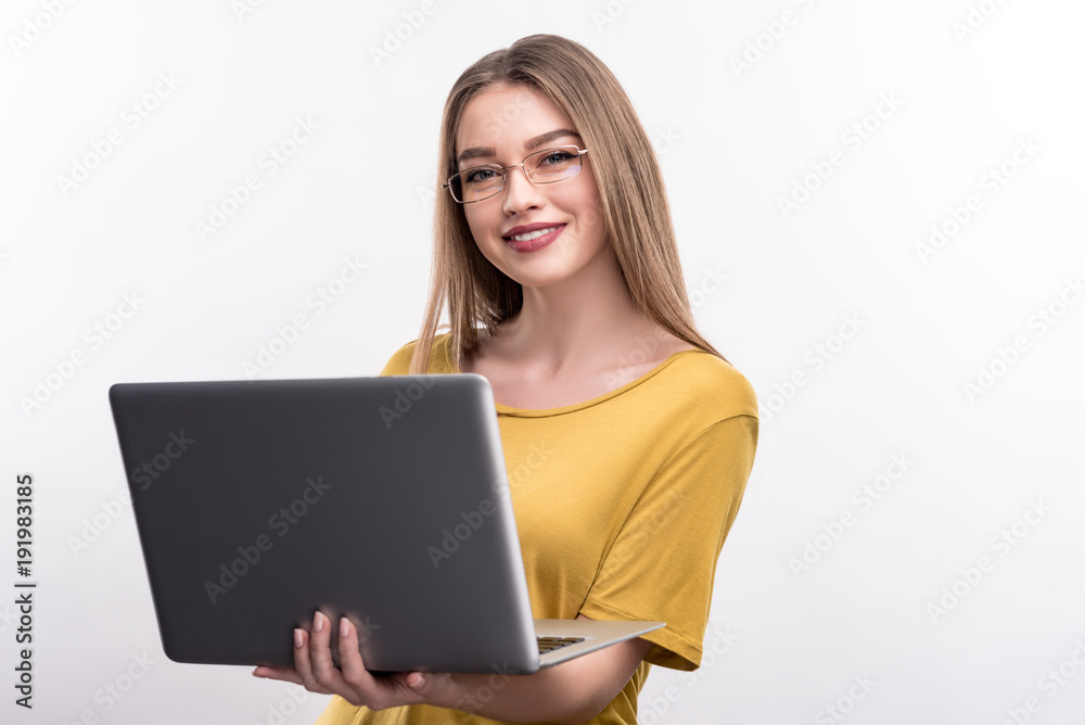 Young professional. Cheerful pretty woman in a mustard blouse holding a laptop and posing with it, isolated on a white background, while wearing eyeglasses Young professional. Cheerful pretty woman in a mustard blouse holding a laptop and posing with it, isolated on a white background, while wearing eyeglasses