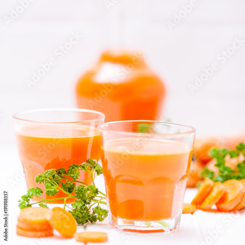 Carrot juice in beautiful glasses, cut orange vegetables and green parsley on white wooden background. Fresh orange drink. Close up photography. Selective focus. Horizontal banner