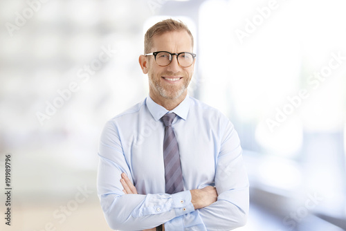 Executive businessman at the office. Smiling senior investment advisor business man wearing shirt and tie while standing at the office and looking at camera. photo
