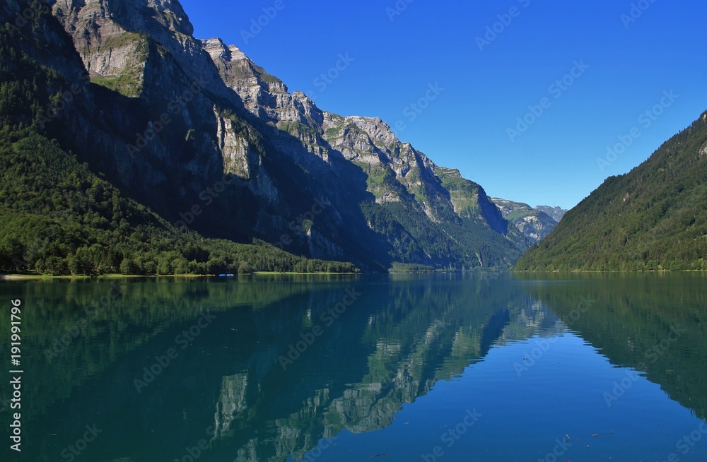 Fototapeta premium Glarnisch, mountain range in Glarus canton reflecting in lake Klontalersee. Quiet summer day in Switzerland.