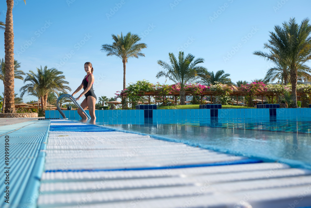 Young woman comes out of the sports pool in a beautiful piece-work swimsuit. Active rest of modern people at the resort. Young woman comes out of the sports pool in a beautiful piece-work swimsuit. Active rest of modern people at the resort.
