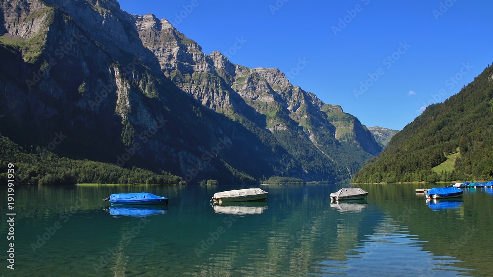Summer day at lake Klontalersee, Switzerland. Fishing boats. Glaernisch, mountain range.
