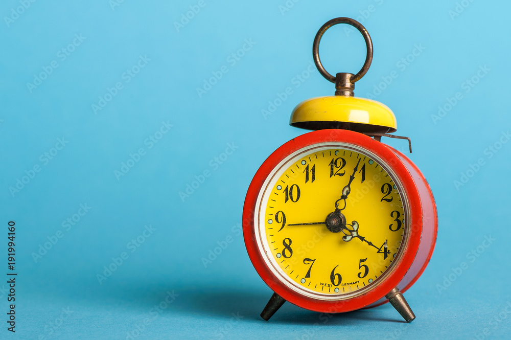 old, colorful alarm clock, in front of blue background old, colorful alarm clock, in front of blue background