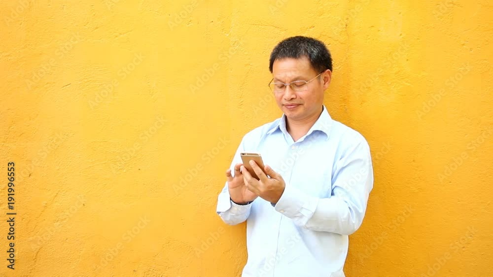 Thai man playing phone with yellow wall Thai man playing phone with yellow wall