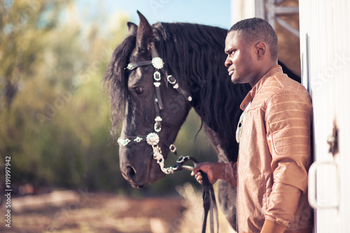 african Man wearing sunglasses near a black horse in hangar