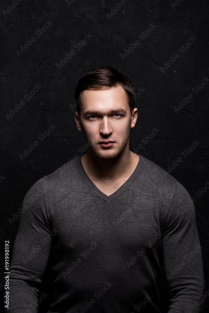 Handsome tough guy on a black background. Portrait. Brawn. Gray sweater. Force. Masculinity. Handsome tough guy on a black background. Portrait. Brawn. Gray sweater. Force. Masculinity.