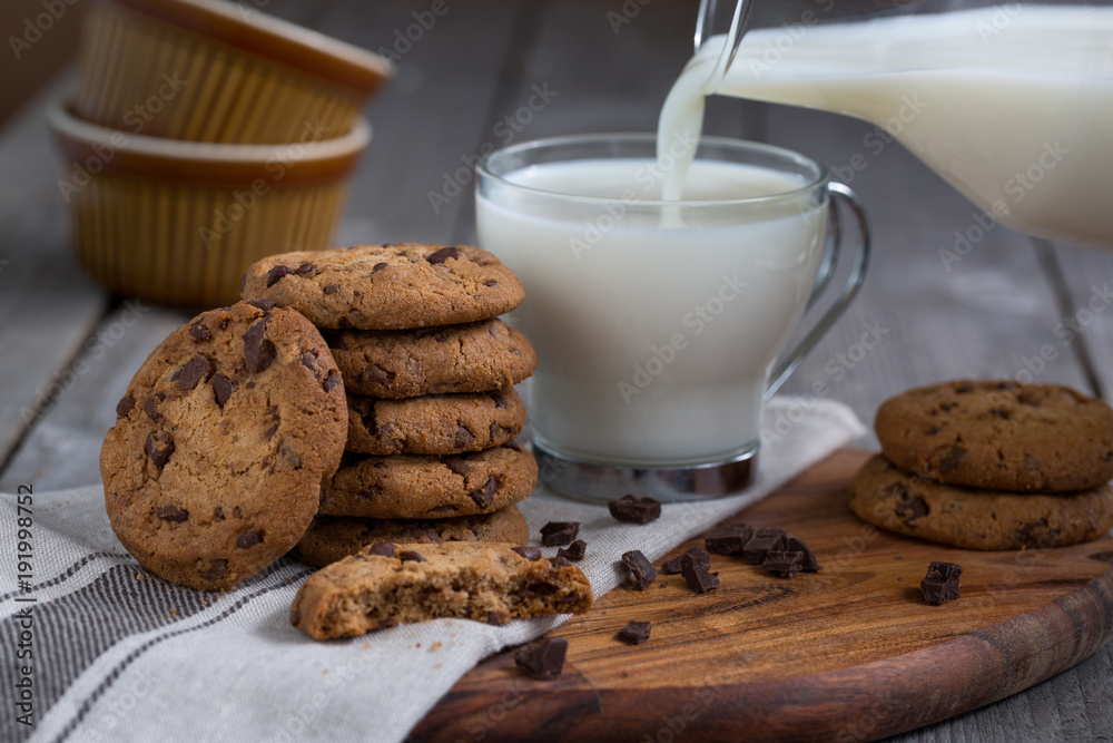 Chocolate chip cookies with milk on old rustic wooden table. Milk pouring. Chocolate chip cookies with milk on old rustic wooden table. Milk pouring.
