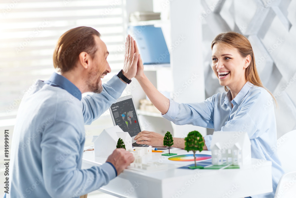 Good job. Beautiful exuberant fair-haired young woman smiling and giving a high-five to her colleague while they working on the project Good job. Beautiful exuberant fair-haired young woman smiling and giving a high-five to her colleague while they working on the project