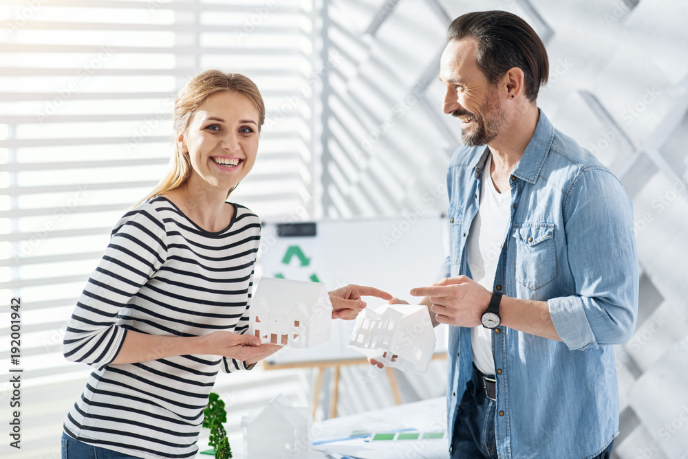 Amazing day. Merry professional young architects smiling and holding house miniatures and a man looking at the woman Amazing day. Merry professional young architects smiling and holding house miniatures and a man looking at the woman