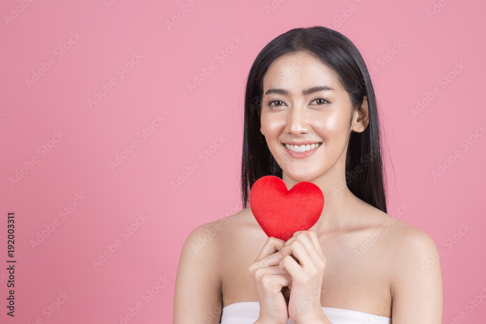 Portrait of Beautiful Asian Woman holding red heart symbol. Beautiful Woman looking to camera. People with Youth and Skin Care Concept. isolated on pink background. Portrait of Beautiful Asian Woman holding red heart symbol. Beautiful Woman looking to camera. People with Youth and Skin Care Concept. isolated on pink background.