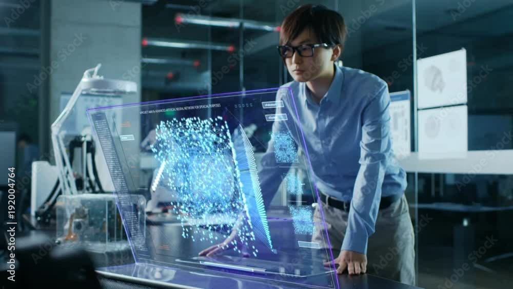 Asian Neural Network Engineer Uses Modern Computer With Transparent Holographic Display. Monitor Shows Interactive Artificial Intelligence Interface . Shot in Modern Glass and Concrete Office.