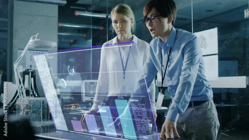 Male and Female Business People Have Discussion while Using Modern Computer With Transparent Holographic Display. Monitor Shows User Interface with Interactive Charts and Graphics.